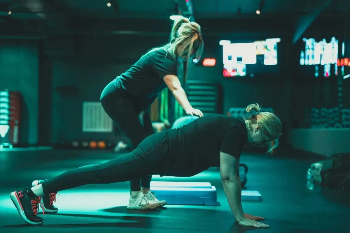 65f07b425ad57b8244598a46 Trainer guiding a client through a plank exercise in the Forward Thinking Fitness studio